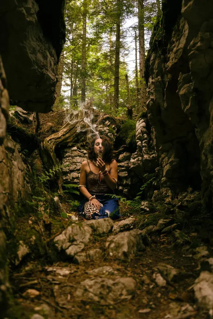 Arianna Zanemvula seduta tra le rocce del bosco, avvolta dal fumo di una pianta